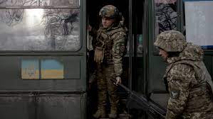 دو سرباز با یونیفورم در حال بار کردن اسلحه در یک کامیون نظامی با پرچم اوکراین.